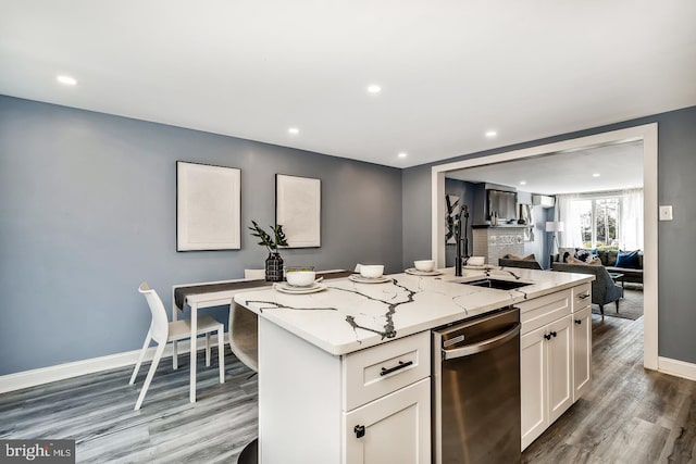 kitchen with wood finished floors, stainless steel dishwasher, white cabinets, a kitchen island with sink, and light stone countertops