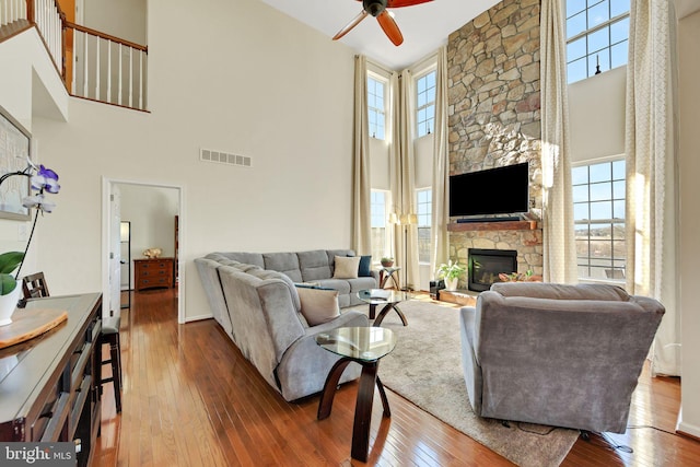 living room featuring visible vents, a high ceiling, a fireplace, ceiling fan, and hardwood / wood-style flooring