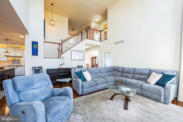 living area with visible vents, a towering ceiling, and wood finished floors