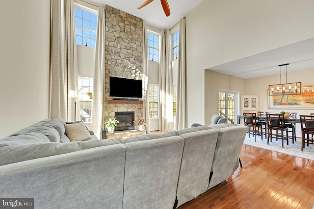 living room featuring ceiling fan with notable chandelier, a fireplace, a towering ceiling, and wood-type flooring