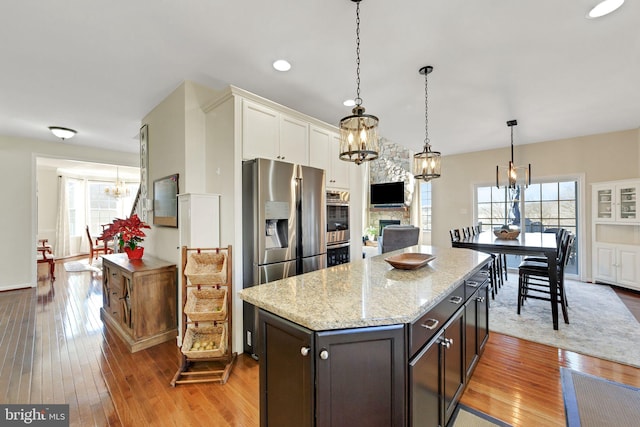 kitchen featuring a notable chandelier, white cabinetry, light wood-style floors, a stone fireplace, and a healthy amount of sunlight