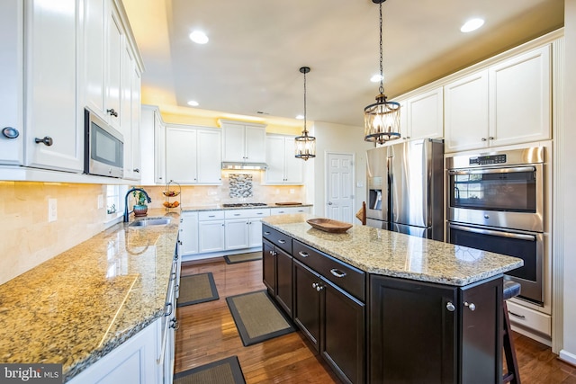 kitchen with a sink, a center island, appliances with stainless steel finishes, white cabinets, and dark wood-style flooring