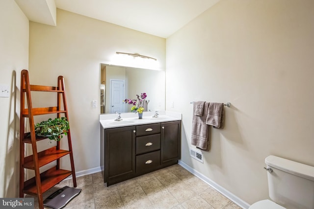 bathroom featuring double vanity, toilet, baseboards, and a sink