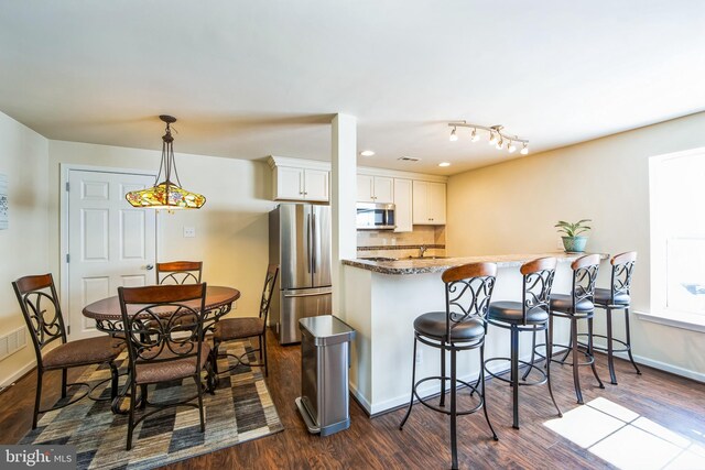 kitchen featuring a breakfast bar, a peninsula, stainless steel appliances, dark wood-type flooring, and white cabinetry