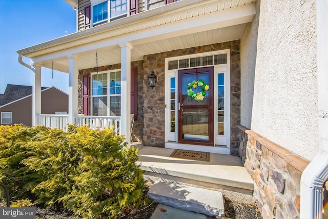 view of exterior entry with stone siding, stucco siding, and a porch