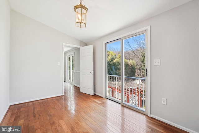 spare room with hardwood / wood-style floors, lofted ceiling, baseboards, and an inviting chandelier