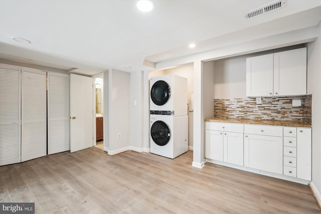 clothes washing area with visible vents, light wood-type flooring, stacked washer / drying machine, and laundry area