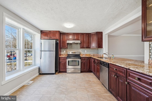 kitchen with under cabinet range hood, dark brown cabinets, appliances with stainless steel finishes, and backsplash