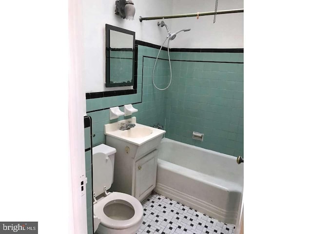 full bathroom with toilet, vanity, tile walls, tile patterned floors, and washtub / shower combination