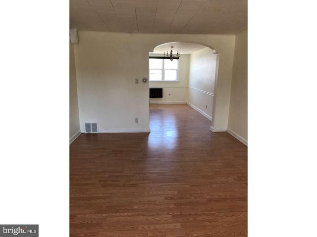 unfurnished room featuring baseboards, visible vents, arched walkways, wood finished floors, and a notable chandelier