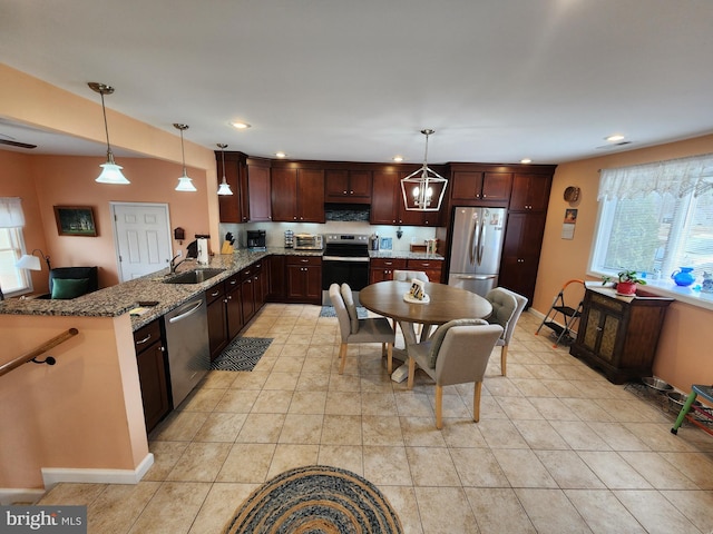 kitchen featuring pendant lighting, a sink, appliances with stainless steel finishes, a peninsula, and light stone countertops