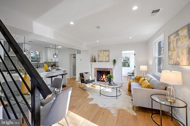 living area with recessed lighting, wood finished floors, visible vents, stairway, and a brick fireplace