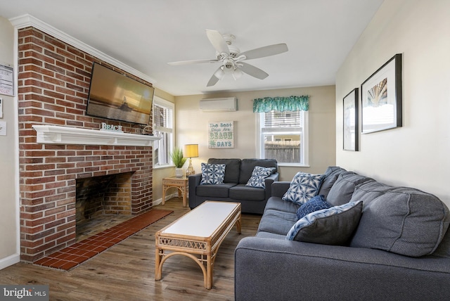 living area with a brick fireplace, ceiling fan, baseboards, a wall unit AC, and wood finished floors