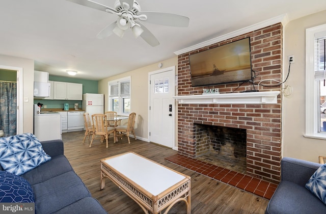 living area featuring ceiling fan, a brick fireplace, baseboards, and wood finished floors