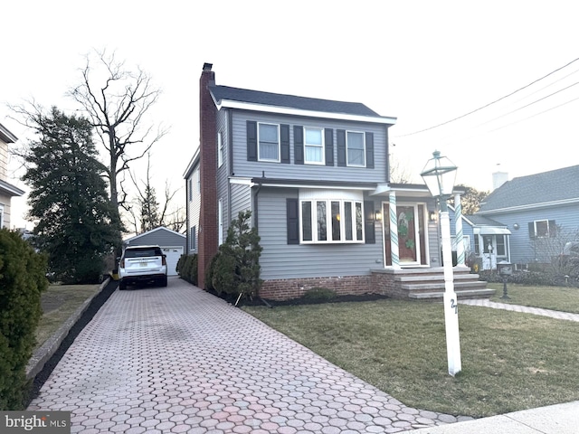 traditional home with an outdoor structure, decorative driveway, a front yard, and a chimney