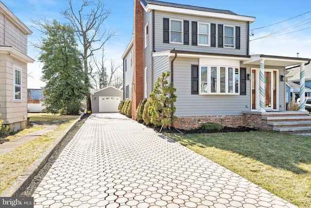 view of front of house featuring decorative driveway, a detached garage, an outdoor structure, a front yard, and a chimney