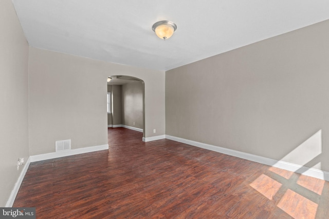 unfurnished room featuring visible vents, arched walkways, baseboards, and dark wood-style floors