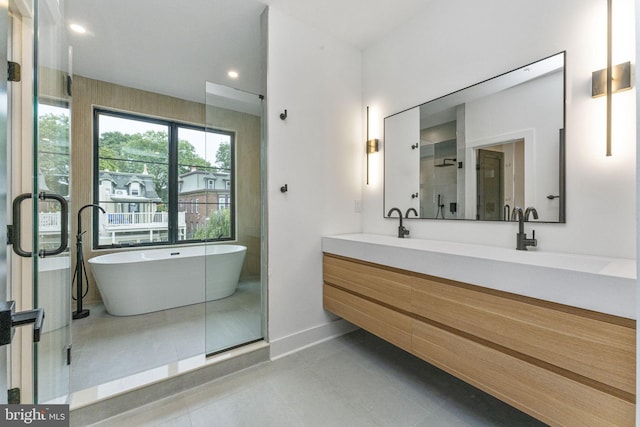 bathroom with a sink, a shower stall, double vanity, baseboards, and a soaking tub