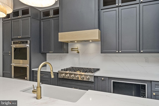 kitchen featuring tasteful backsplash, glass insert cabinets, light stone counters, appliances with stainless steel finishes, and a sink