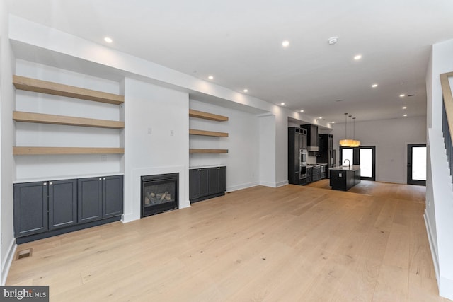 unfurnished living room with built in features, visible vents, light wood finished floors, recessed lighting, and a glass covered fireplace