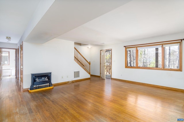 unfurnished living room with baseboards, stairs, visible vents, and wood finished floors