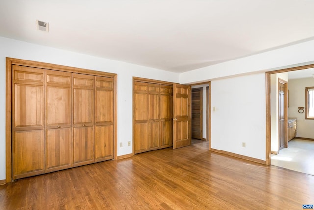 unfurnished bedroom with multiple closets, baseboards, visible vents, and wood finished floors