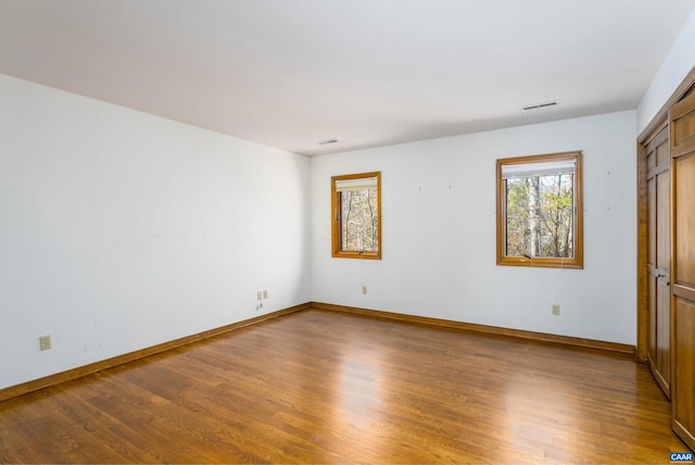 spare room with wood finished floors, visible vents, and baseboards