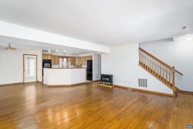 unfurnished living room with stairway, baseboards, visible vents, and wood finished floors