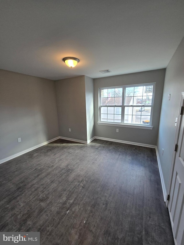 empty room featuring dark wood-style flooring, visible vents, and baseboards