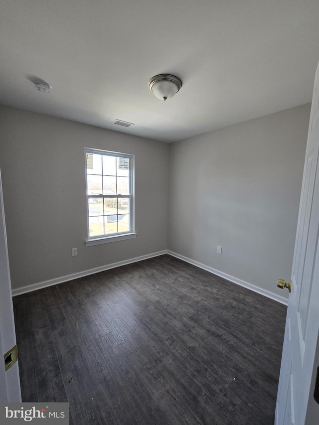 unfurnished room featuring visible vents, dark wood finished floors, and baseboards