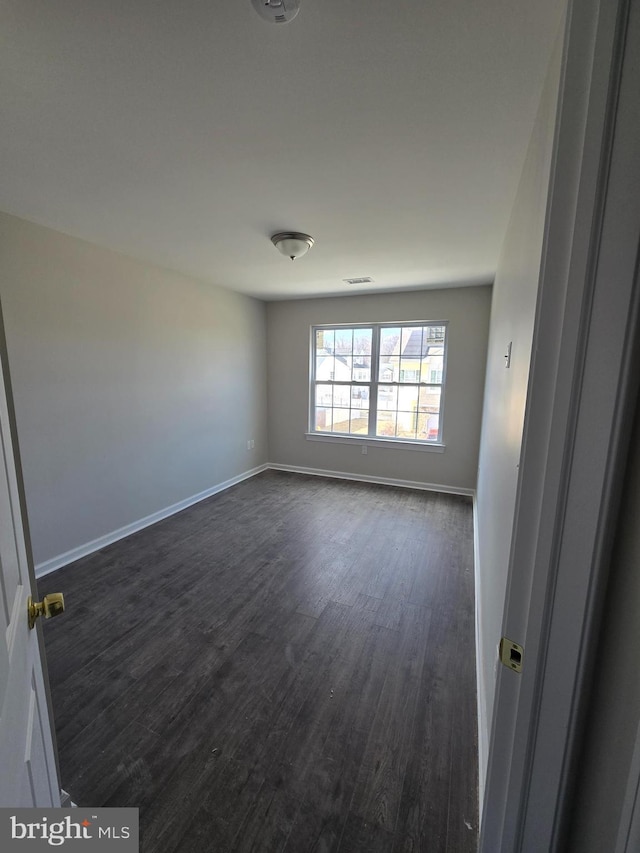 empty room with dark wood-style flooring, visible vents, and baseboards