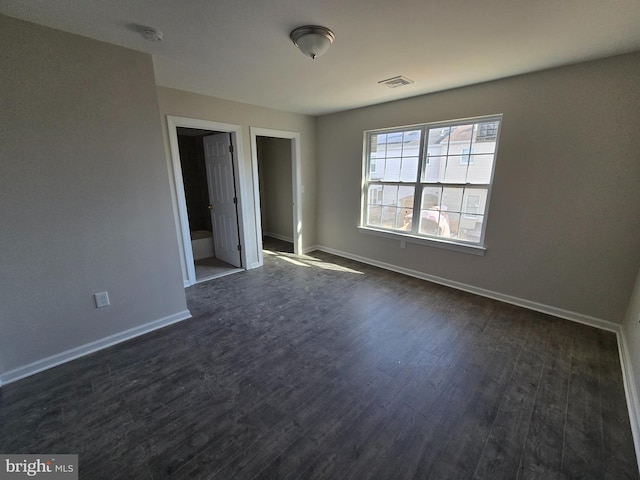 unfurnished room with dark wood-type flooring, visible vents, and baseboards