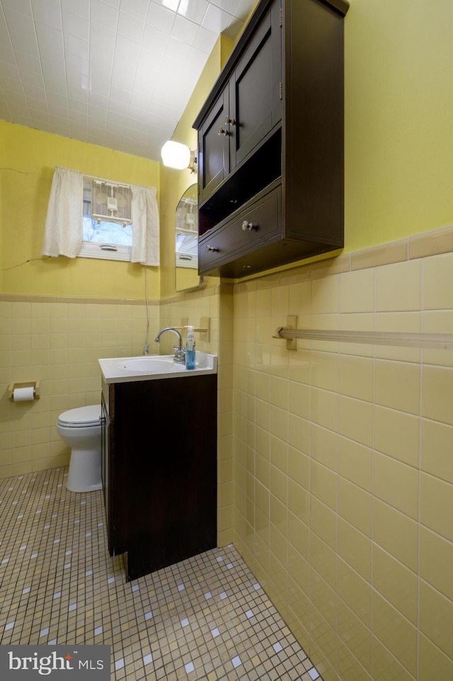 bathroom with wainscoting, toilet, tile patterned flooring, vanity, and tile walls