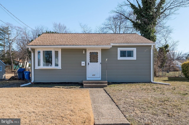 bungalow-style home with fence, a front lawn, and roof with shingles