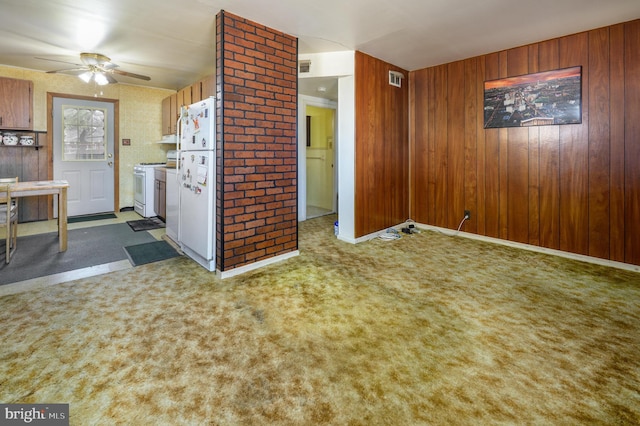 interior space with carpet floors, wood walls, visible vents, a ceiling fan, and baseboards