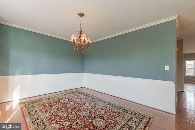 spare room featuring crown molding, wood finished floors, and a chandelier