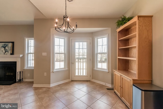 doorway to outside featuring a glass covered fireplace, an inviting chandelier, light tile patterned floors, and a wealth of natural light