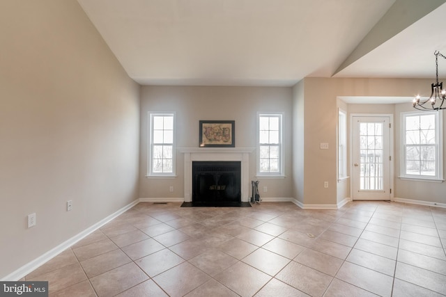 unfurnished living room with baseboards, a fireplace with flush hearth, vaulted ceiling, light tile patterned flooring, and a notable chandelier