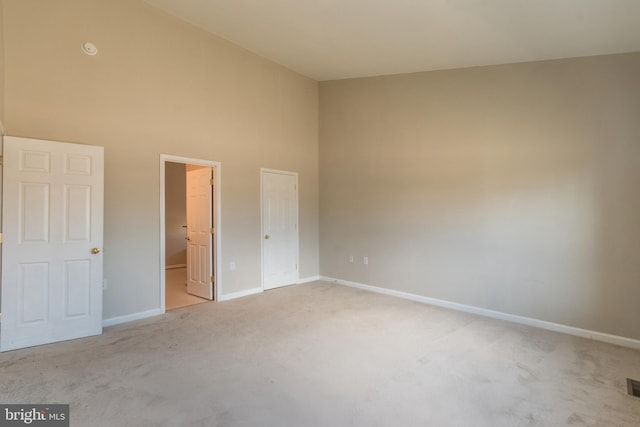 unfurnished bedroom featuring light colored carpet, visible vents, baseboards, and a towering ceiling