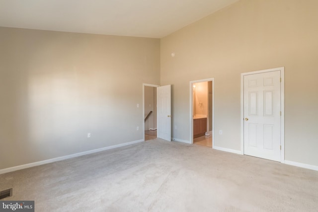 unfurnished bedroom featuring visible vents, baseboards, carpet floors, ensuite bathroom, and high vaulted ceiling