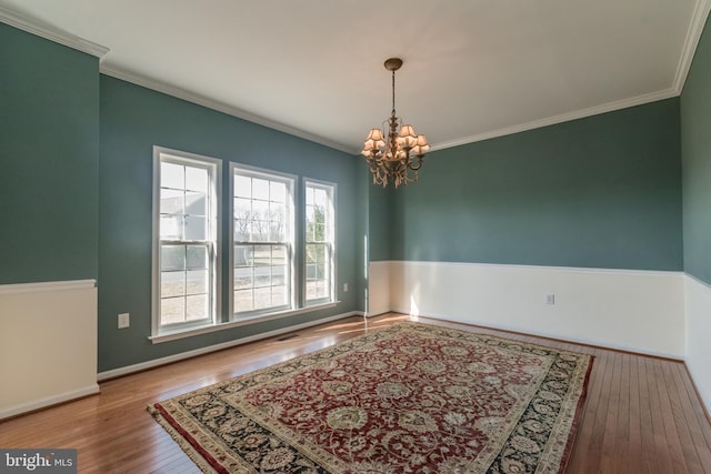 unfurnished room featuring a notable chandelier, crown molding, baseboards, and wood-type flooring