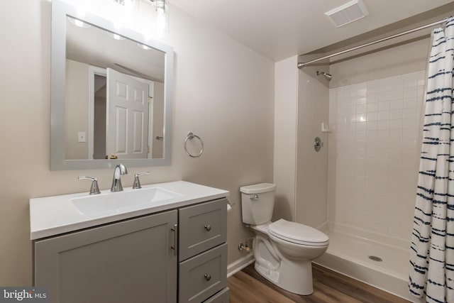 bathroom with visible vents, toilet, wood finished floors, a tile shower, and vanity