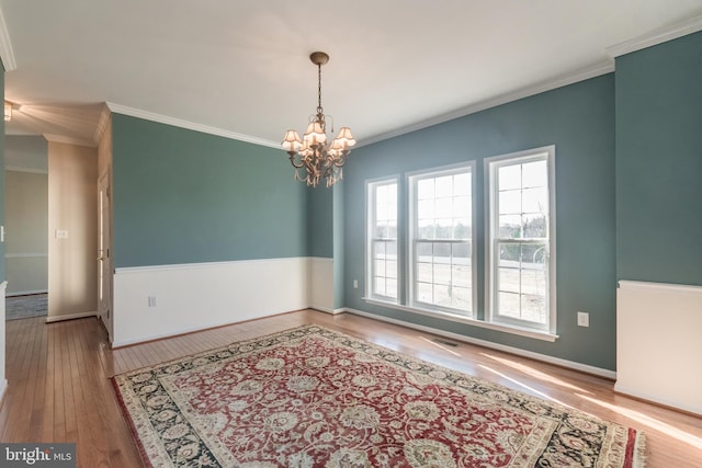 unfurnished room featuring crown molding, wood finished floors, baseboards, and a chandelier