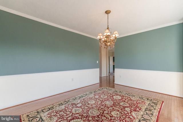 empty room with a notable chandelier, ornamental molding, a wainscoted wall, and hardwood / wood-style floors