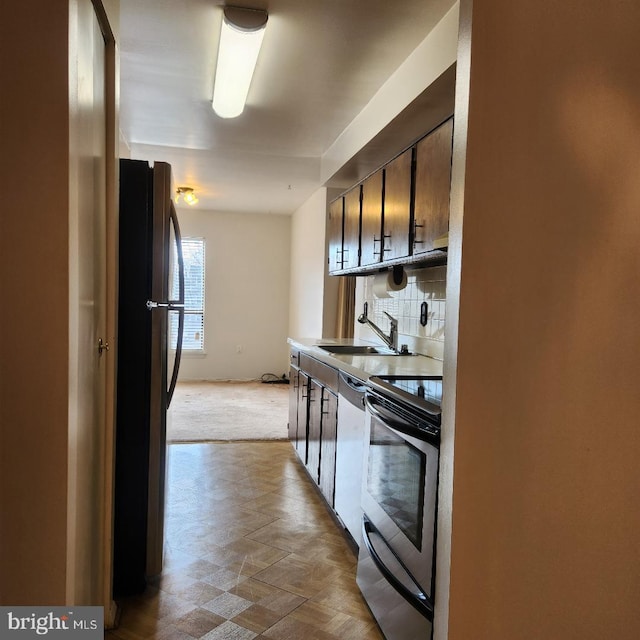 kitchen featuring dishwashing machine, a sink, freestanding refrigerator, tasteful backsplash, and stainless steel range with electric stovetop