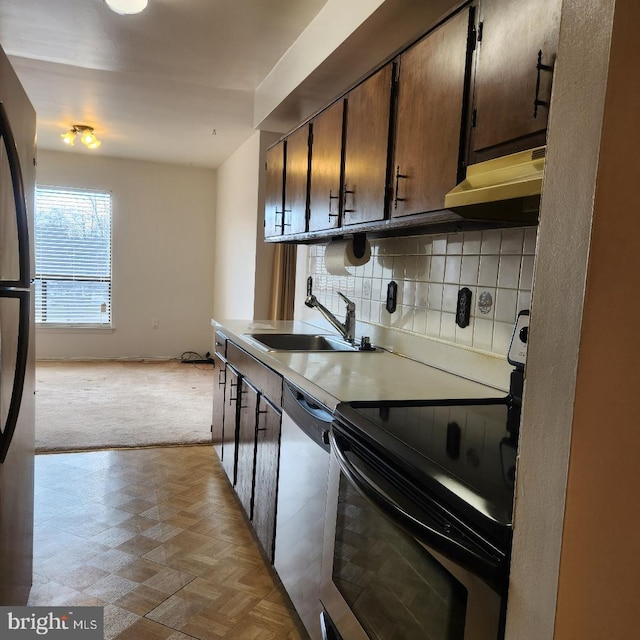 kitchen featuring dark brown cabinetry, under cabinet range hood, a sink, appliances with stainless steel finishes, and tasteful backsplash