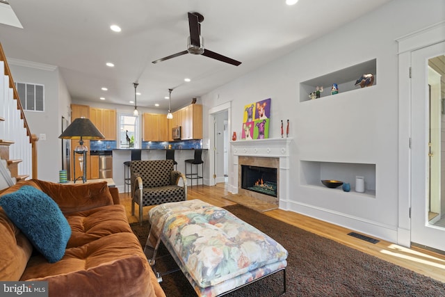 living room featuring stairway, a fireplace with flush hearth, light wood-style floors, and visible vents