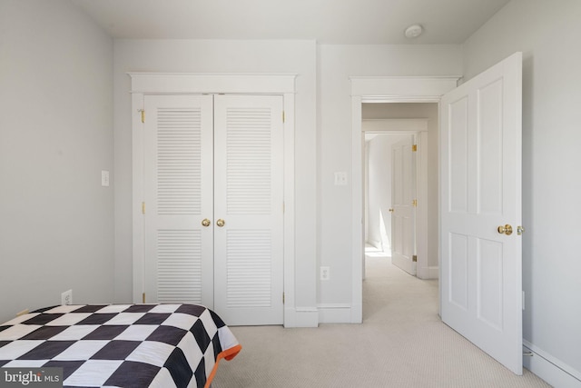 bedroom with a closet, light carpet, and baseboards
