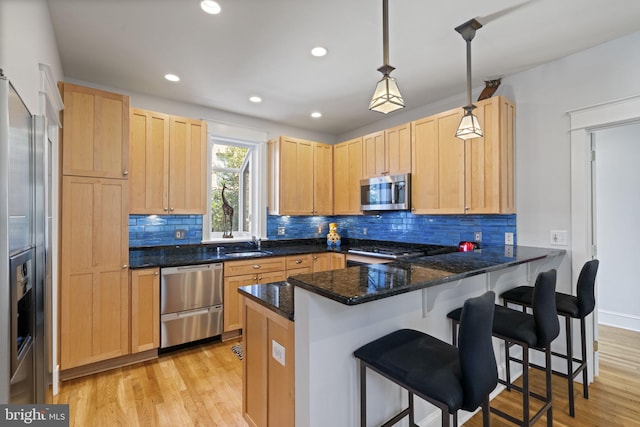 kitchen with light brown cabinets, appliances with stainless steel finishes, light wood-style floors, and a peninsula