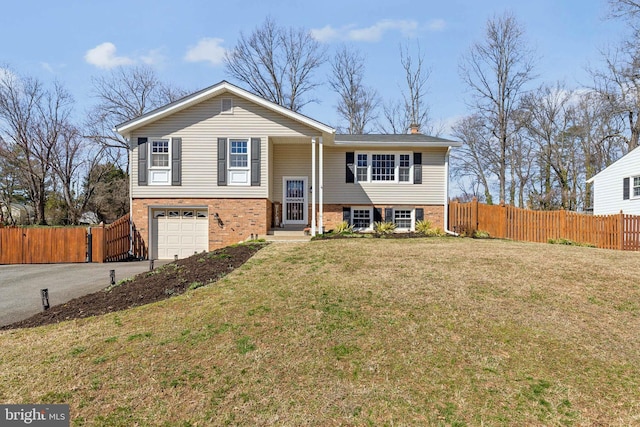 split foyer home with fence, driveway, an attached garage, a front lawn, and brick siding